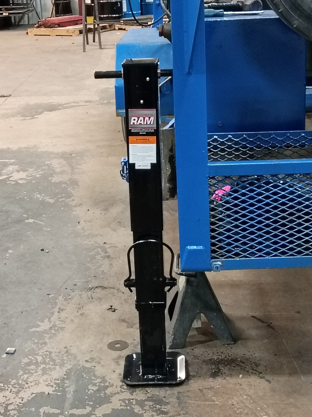 A black trailer jack beside blue workshop equipment.