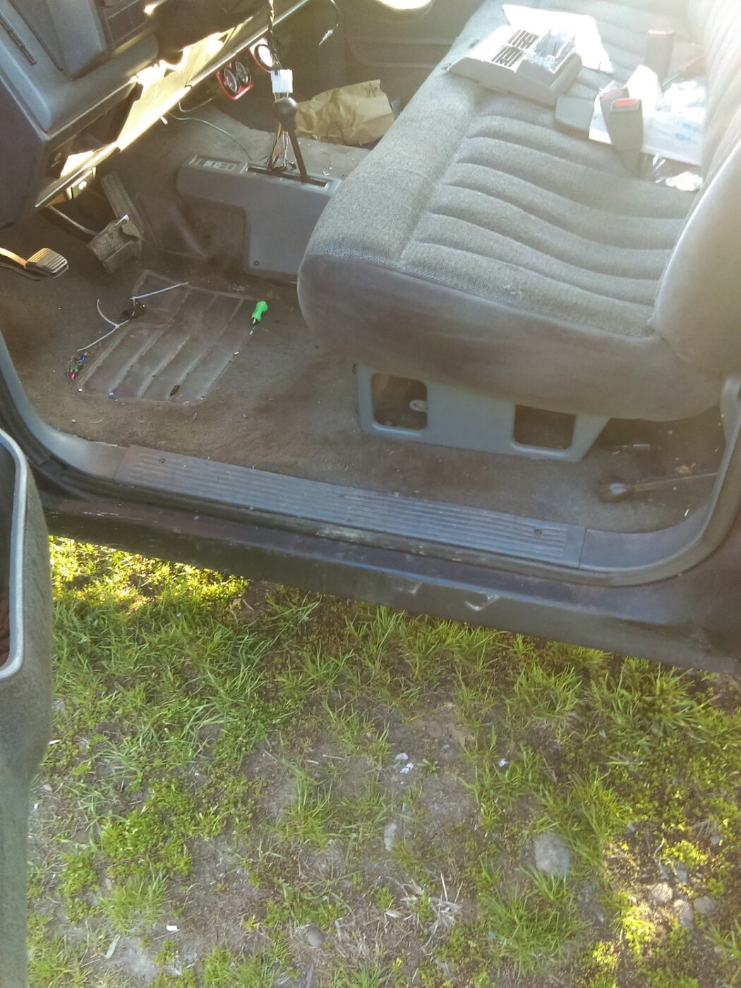 A pickup cab with a gray bench seat, exposed floor section, and tools inside.