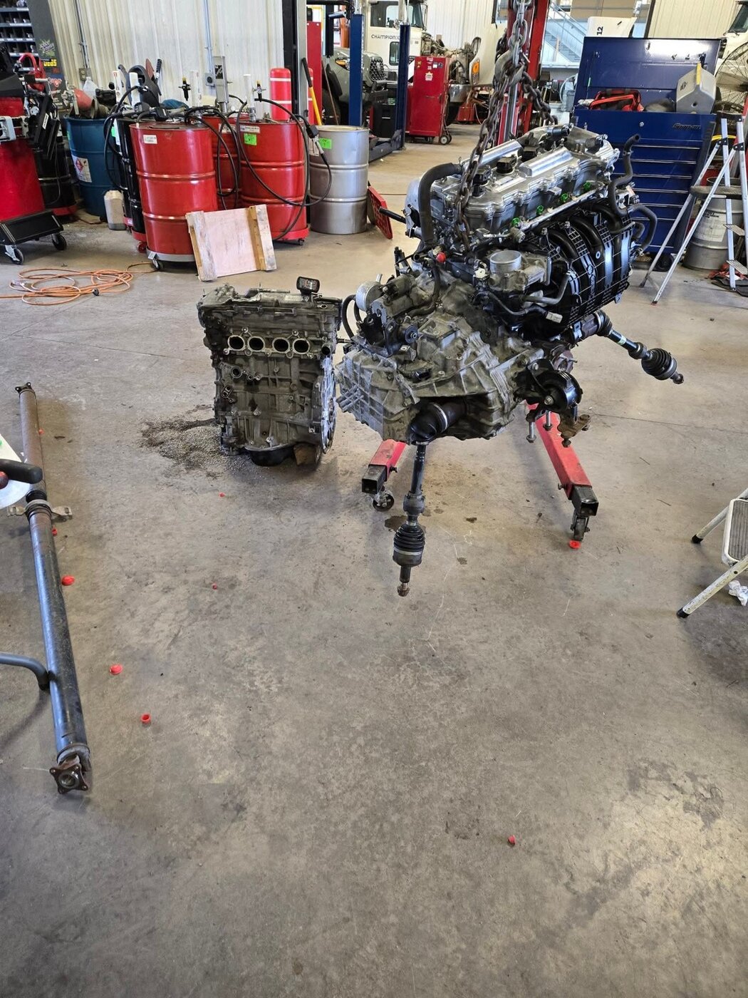 An engine on a stand with other components on the workshop floor.