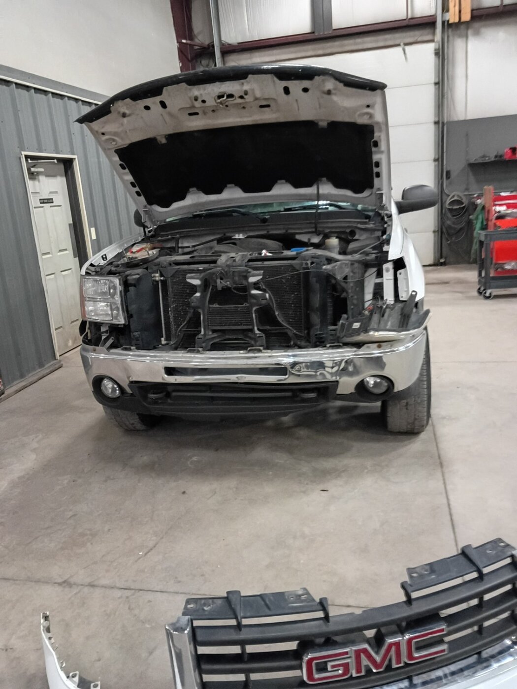 A white pickup with front trim removed and the hood open.