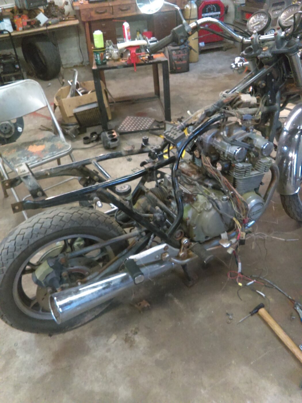 A motorcycle with its tank and seat removed, showing the frame, engine, and wiring.