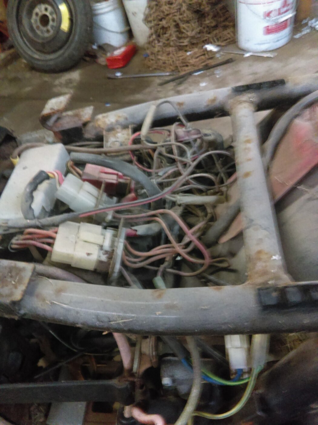 A close view of wiring and electrical connectors beneath a motorcycle seat area.