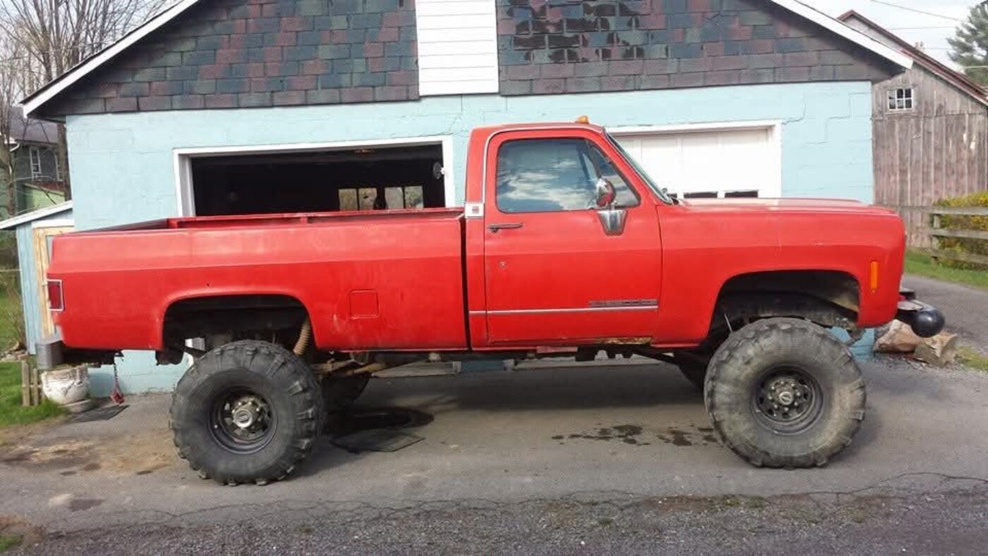 A red lifted pickup parked beside a garage.